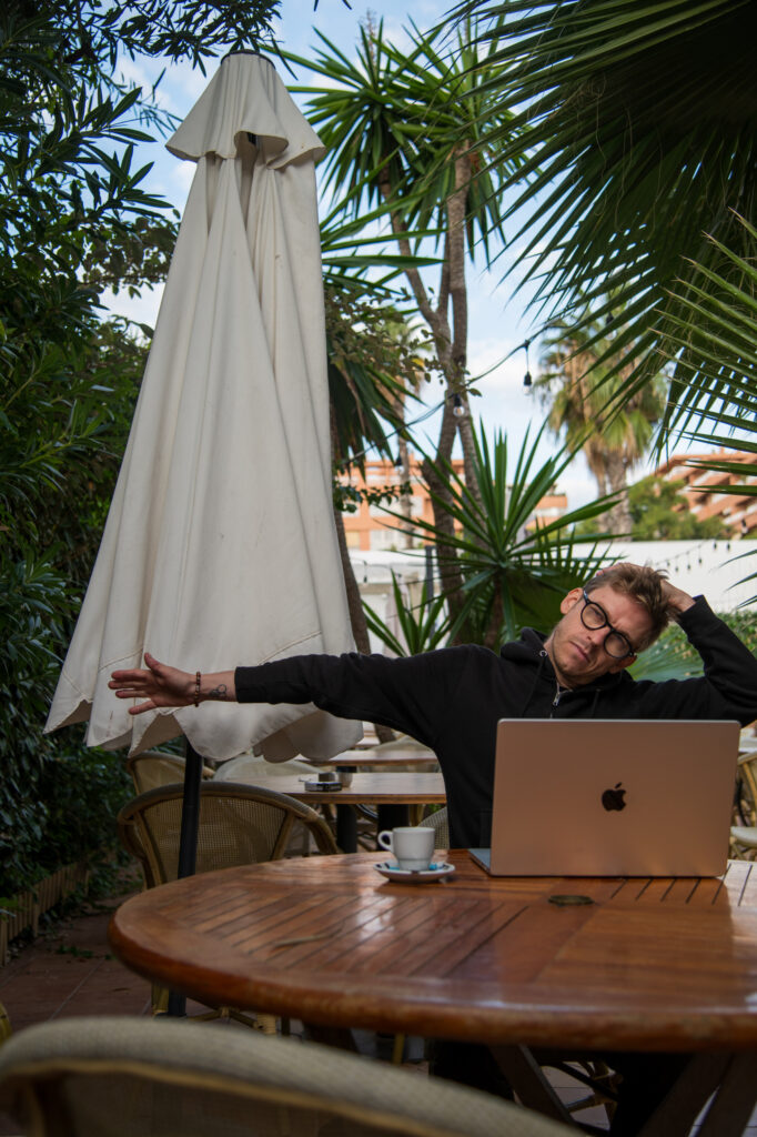 A remote worker practicing mindful stretching and self-regulation during a work break at an outdoor table with a laptop.